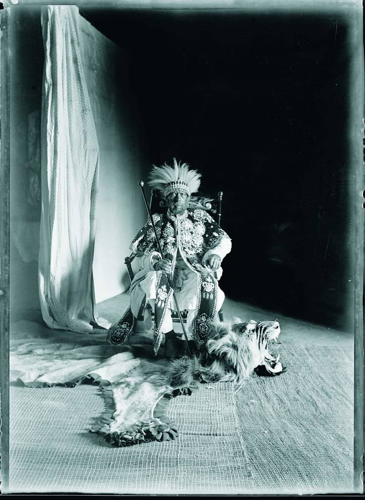 An aged photograph capturing Emperor Menelik II in a costume, calmly sitting on the floor.