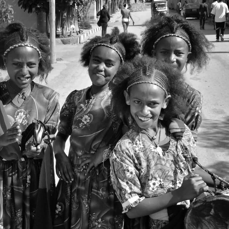 Three young girls in traditional dress, smiling. Celebrating Ashenda, a cultural festival in Ethiopia.