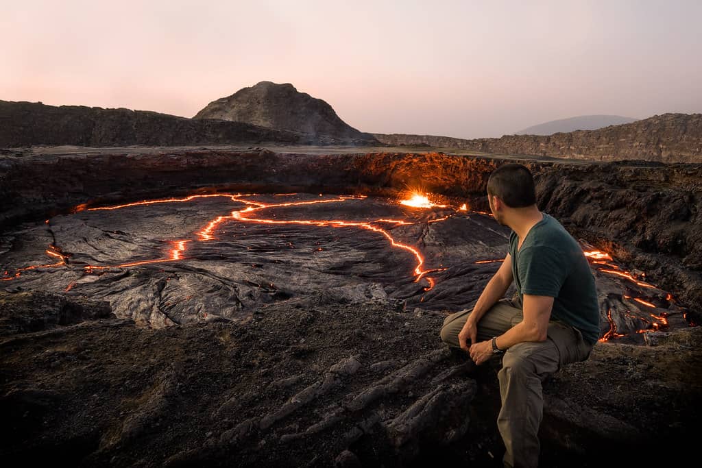 Person sitting on rock, admiring lava pit during Erta Ale visit.