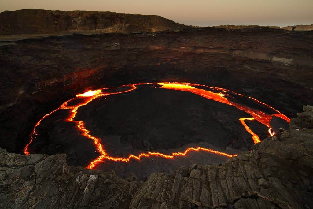 Aerial view of Erta Ale volcano, showcasing a vast crater with molten lava streaming into it.