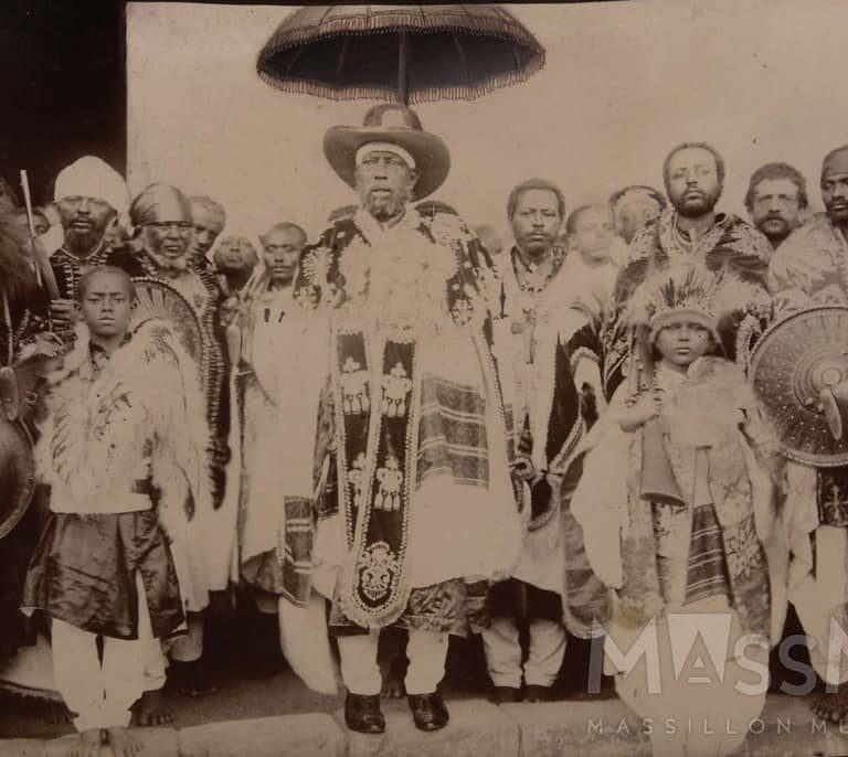 A vintage photo of people in traditional attire, with Emperor Menelik II standing in the center.