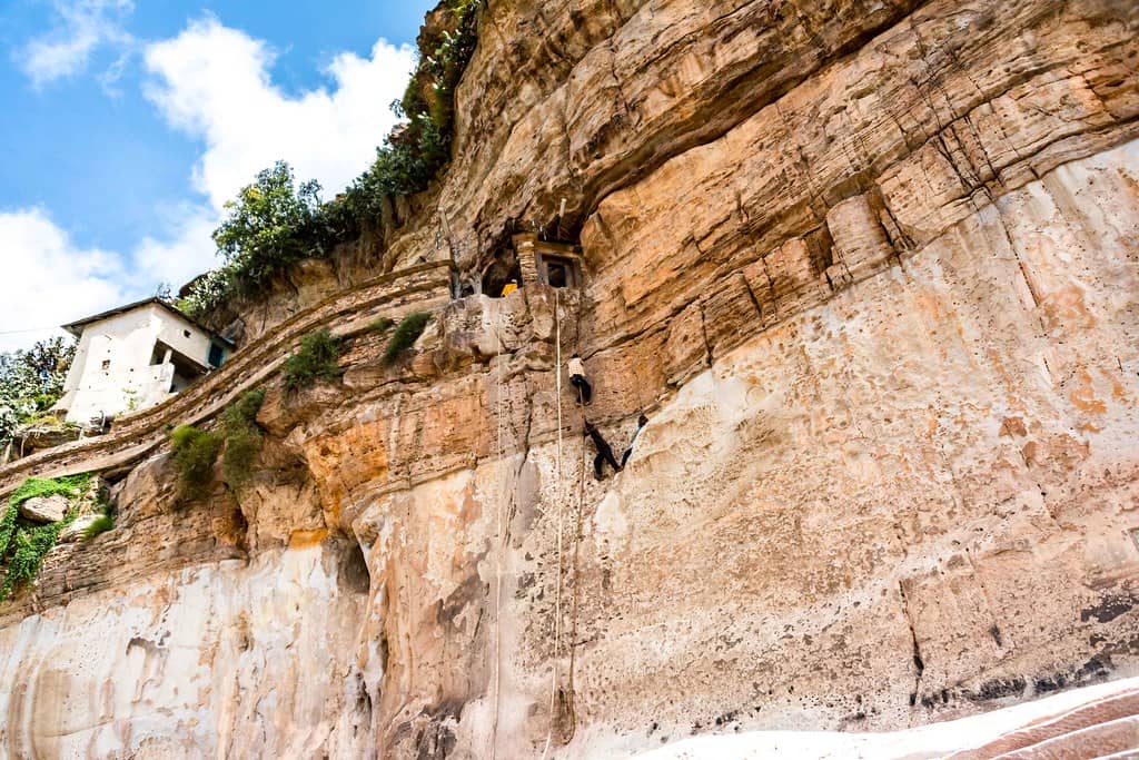 A man ascending a cliff using a ladder at Debre Damo Monastery.