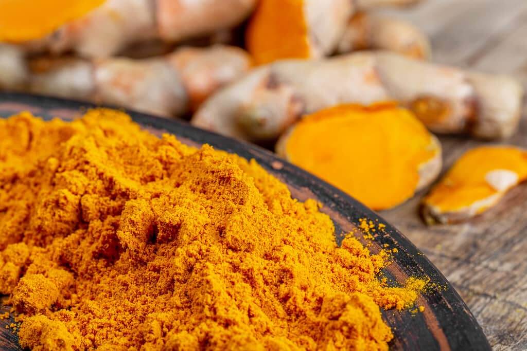 A close-up image of turmeric powder and turmeric root, commonly used in cooking and known for its vibrant yellow color.