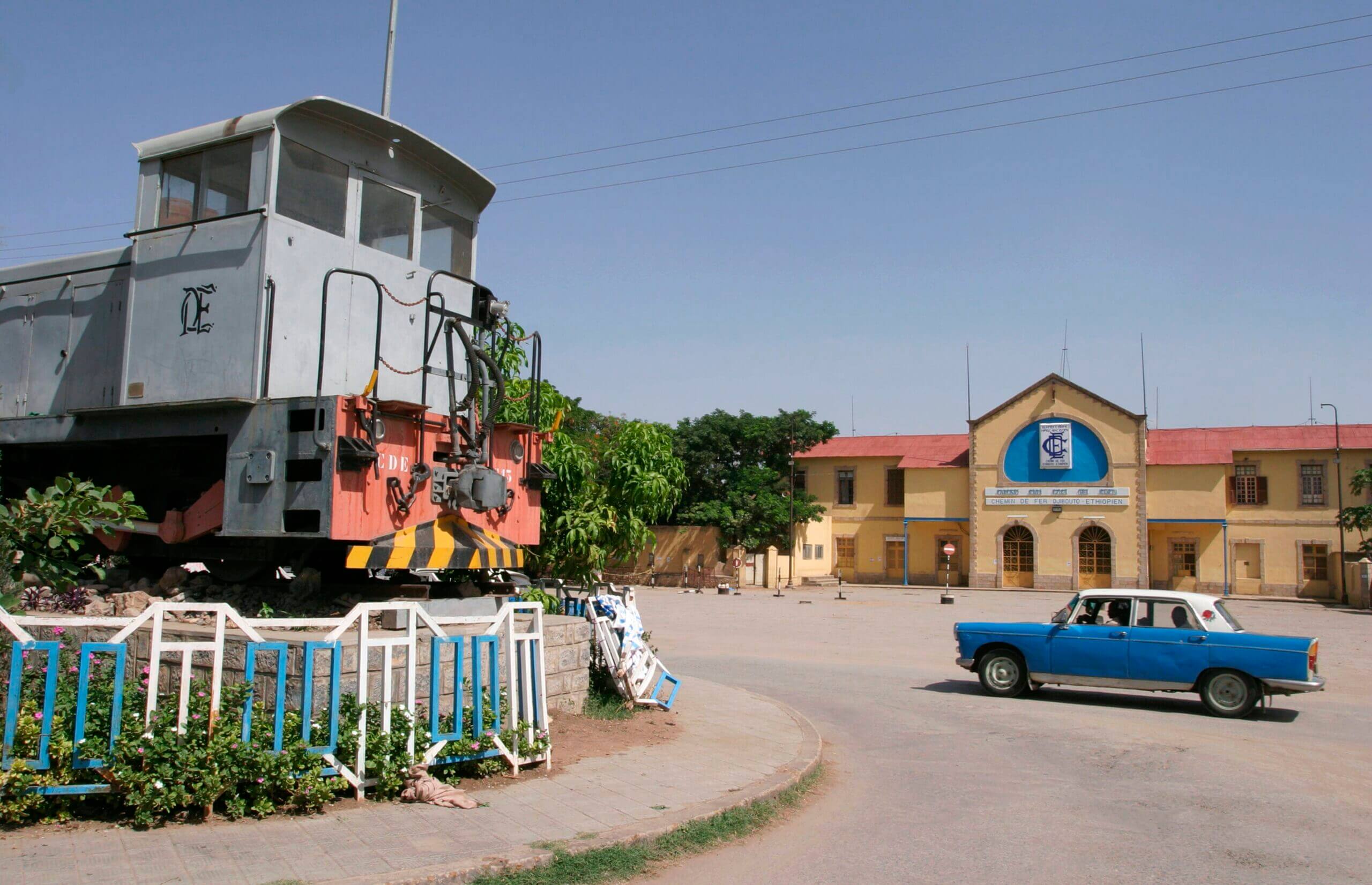 A parked blue car beside a train dire dawa, creating a vibrant contrast between the two modes of transportation.